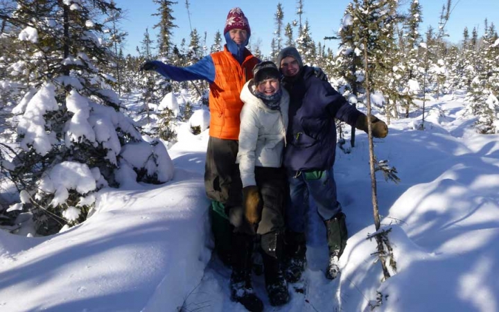 three people stand in deep snow surrounded by trees and smile at the camera 